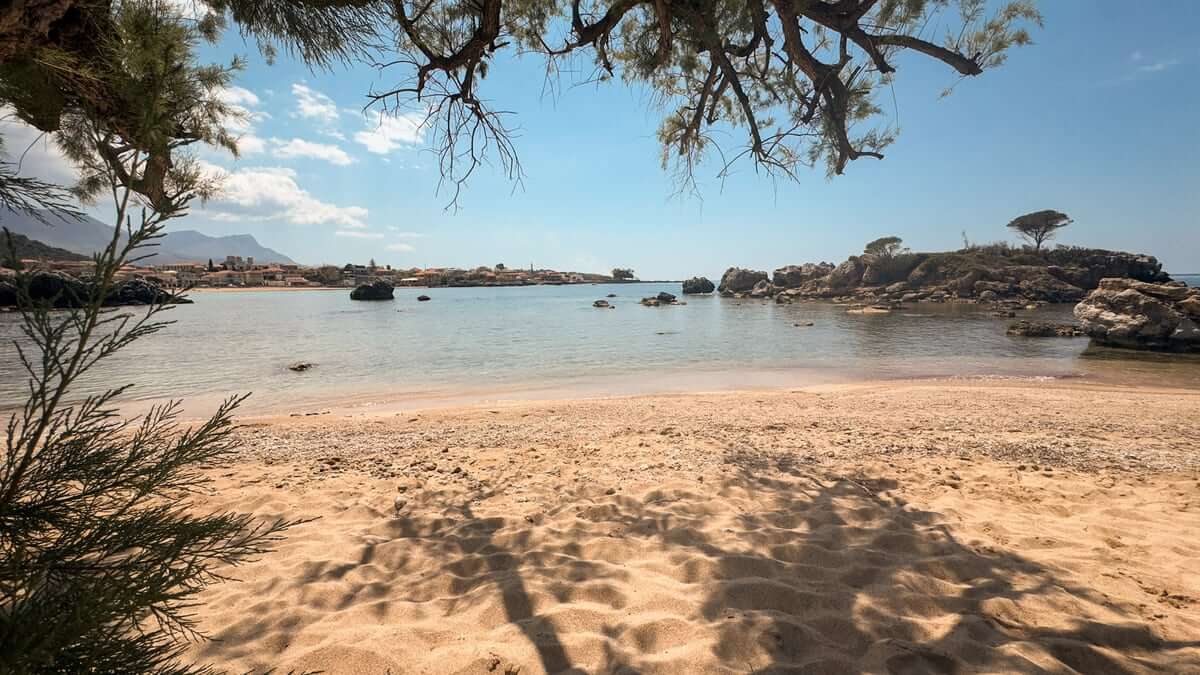 Sandstrand in der Mani mit ruhigem Wasser, Felsen und Schatten der Bäume